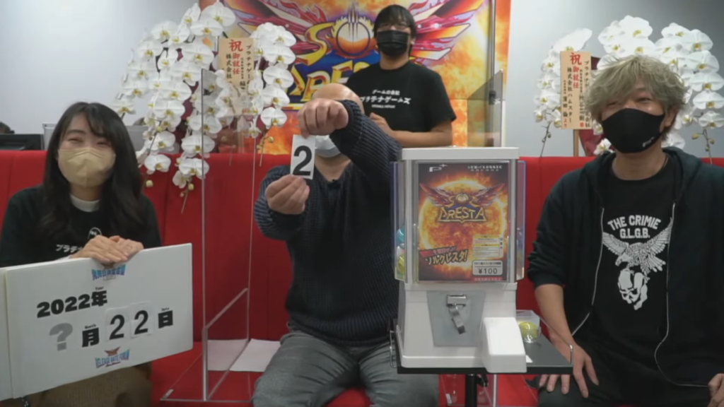 Sol Cresta team showing off the release date using a gacha machine.